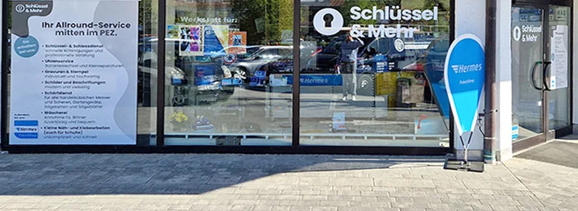 Schaufenster von Schlüssel & Mehr im PEZ mit dem Schriftzug an der Scheibe und dem Aufsteller des Hermes Paketshops.